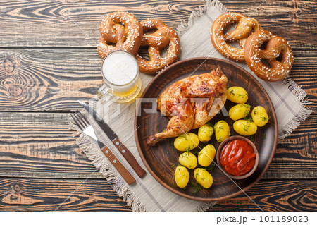 Grilled half chicken with boiled potatoes and tomato sauce served with beer and pretzel closeup. Horizontal top view Grilled half chicken with boiled potatoes and tomato sauce served with beer and pretzel closeup. Horizontal top view 101189023