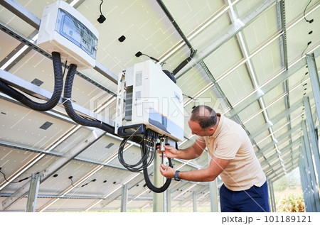 Young man adjusting hybrid inverter. Worker connecting wires to PV battery. Alternative energy in nowadays. 101189121