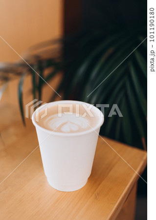 White Paper cup of coffee with latte art on wooden table. Street coffee, top view. Cup coffee in palm branches and leaves. Delicious hot beverage. Blank space for text, mockup 101190180