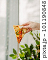 A piece of pizza in his hand, against the backdrop of the restaurant, Side view of the pizza. The concept of Italian cuisine, street food, fast food, fast food. Banner 101190848