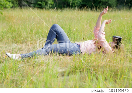 Young beautiful woman wearing virtual reality glasses lying on a meadow in the park Young beautiful woman wearing virtual reality glasses lying on a meadow in the park 101195470