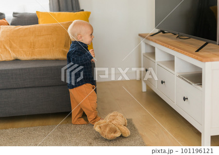 Toddler boy laughing having fun standing near sofa in living room at home copy space. Adorable baby making first steps alone. Happy childhood and child care concept Toddler boy laughing having fun standing near sofa in living room at home copy space. Adorable baby making first steps alone. Happy childhood and child care concept 101196121