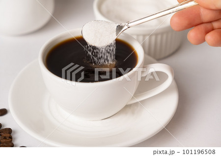 The process of pouring white sugar from a spoon into a white cup of coffee. Sugar addict, diabetes. 101196508