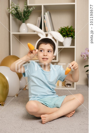 A preschool Easter boy plays with carrots, rabbit ears on his head. 101198677