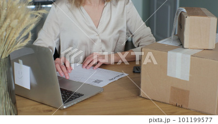 A young woman writes a return order and sits at a table with a laptop at home. Close-up video of a female customer writing on paper and filling out a form, wanting to return a product. 101199577
