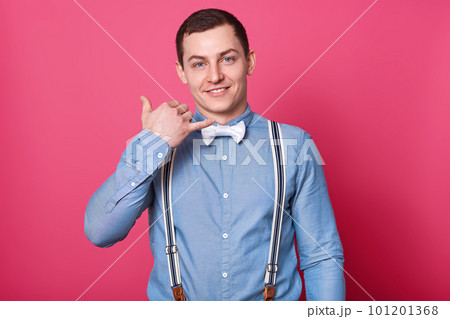 Indoor studio shot of dark haired cheergul young man wearing formal stylish clothes, rising up his arm, makeng mobile phone gesture, looks pleased. People, communication and emotions concept. Indoor studio shot of dark haired cheergul young man wearing formal stylish clothes, rising up his arm, makeng mobile phone gesture, looks pleased. People, communication and emotions concept. 101201368