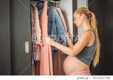 A pregnant woman has nothing to wear. A pregnant woman stands in front of a closet with clothes and does not know what to wear because the clothes do not fit on her A pregnant woman has nothing to wear. A pregnant woman stands in front of a closet with clothes and does not know what to wear because the clothes do not fit on her 101201736
