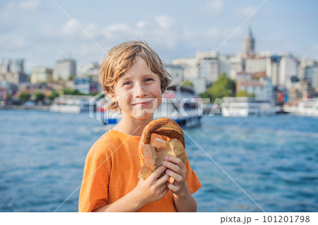 Boy in Istanbul having breakfast with Simit and a glass of Turkish tea. Glass of Turkish tea and bagel Simit against golden horn bay and the Galata Tower in Istanbul, Turkey. Turkiye. Traveling with 101201798