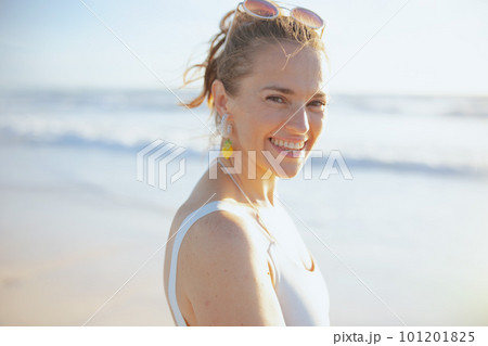 Portrait of smiling stylish woman in white swimwear at beach 101201825