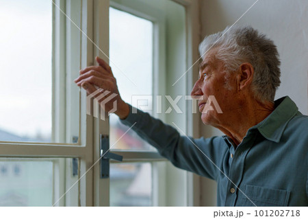 Senior man looking out of window, concept of solitude in retirement. 101202718