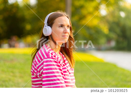 Relaxed woman sitting on the grass listening to music with headphones in a park Relaxed woman sitting on the grass listening to music with headphones in a park 101203025