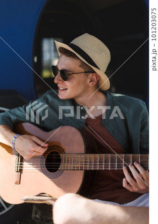Young man sitting in van playing on the guitar and enjoying summer time. Young man sitting in van playing on the guitar and enjoying summer time. 101203075