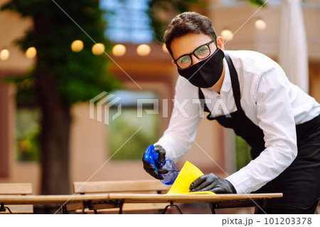 Disinfecting to prevent COVID-19. Waiter in protective face mask and gloves cleaning. 101203378
