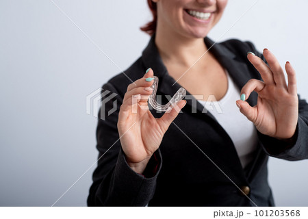 The woman in the jacket shows the ok sign and demonstrates the mouth guards to align the bite. The girl approves of the plastic removable braces for the teeth 101203568
