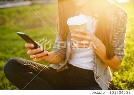 The girl holds the phone and coffee in hand. Sunset. Summertime. 101204358