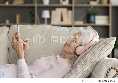 Relaxed elder smartphone user woman in headphones listening to music 101205355
