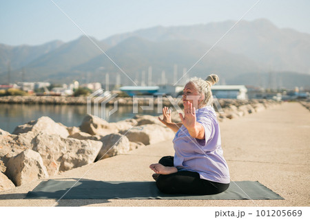 Mature old woman with dreadlocks practicing yoga and tai chi outdoors by the sea - wellbeing and wellness 101205669