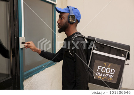Delivery service courier ringing building doorbell side view, waiting for client outdoors. African american deliveryman with thermal backpack standing in front of door, delivering takeaway lunch Delivery service courier ringing building doorbell side view, waiting for client outdoors. African american deliveryman with thermal backpack standing in front of door, delivering takeaway lunch 101206646