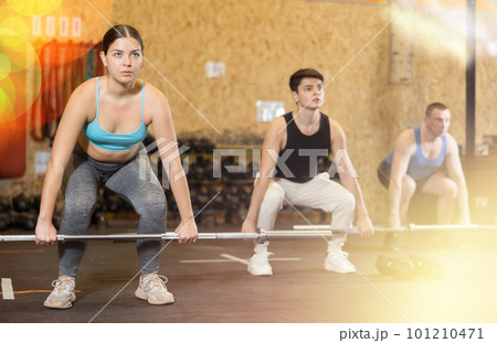 Focused fitness woman in activewear exercising with barbell during group workout in gym health center. CrossFit healthy concept 101210471