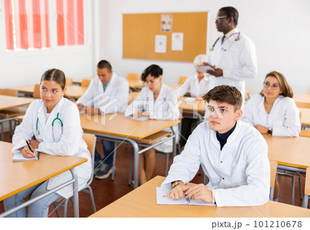 Doctors different age sitting at desk in classroom working during lesson at education class Doctors different age sitting at desk in classroom working during lesson at education class 101210678