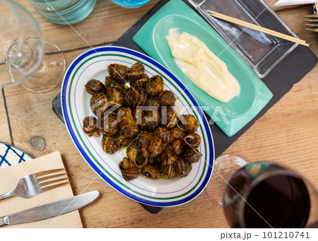 Flavored caracoles(Spanish) snails in shells, served with white sauce and red wine presented in a restaurant Flavored caracoles(Spanish) snails in shells, served with white sauce and red wine presented in a restaurant 101210741
