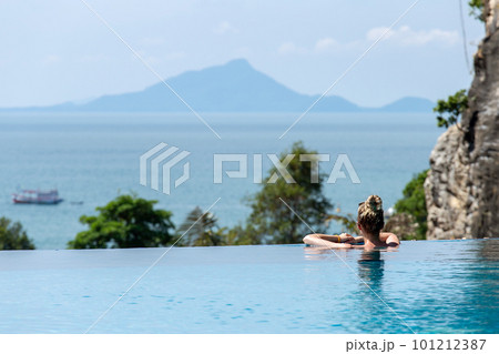 Woman relaxing in infinity swimming pool looking at view 101212387