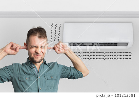 The air conditioner is broken - makes loud noises, noises and vibrations. Man covering his ears The air conditioner is broken - makes loud noises, noises and vibrations. Man covering his ears 101212581