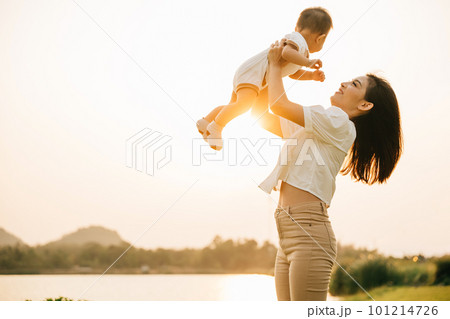 In a carefree summer moment, mom holds her cute toddler son up high, throwing him up into sky. playful child enjoys freedom of flying, while cheerful mother smiles and enjoy moment of family happiness 101214726