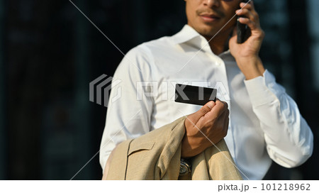 Businesswoman holding credit card, having phone conversation with customer service while standing outside office building 101218962