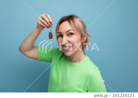 close-up of lucky cute blond woman in casual look holding apartment keychain on blue background 101220221