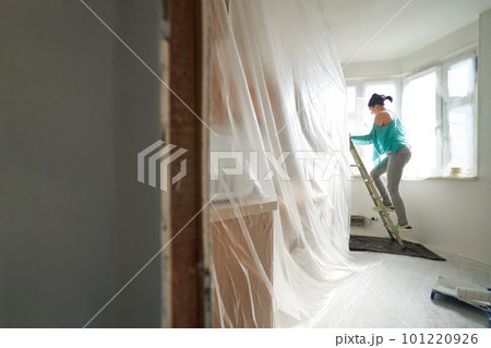Woman stands on the stairs and paints the wall with a roller Woman stands on the stairs and paints the wall with a roller 101220926