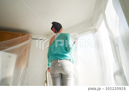 Woman stands on the stairs and paints the wall with a roller 101220928
