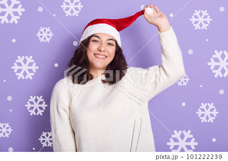 Portrait of charming beautiful brunette touching her hat with one hand, waiting for new year, spending time alone, enjoying winter holidays, having rest, smiling sincerely. Vacation concept. 101222239