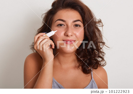 Sstudio shot of girl applying treatment cream from acne, charming smiling female wearing gray sleveless t shirt, having problem skin posing isolated overwhite studio background. Skin care concept. Sstudio shot of girl applying treatment cream from acne, charming smiling female wearing gray sleveless t shirt, having problem skin posing isolated overwhite studio background. Skin care concept. 101222923