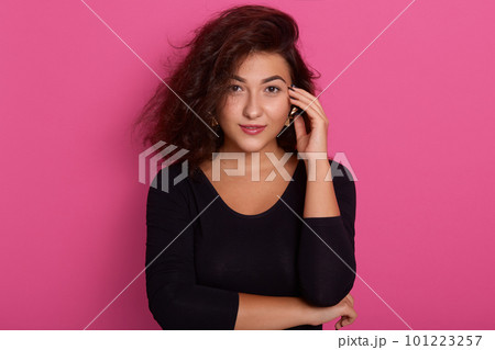 Attractive beautiful brunette woman with perfect skin posing isolated over pink background, wearing black shirt, looking directly at camera, keeping hand on her ear,having pensive facial expression. Attractive beautiful brunette woman with perfect skin posing isolated over pink background, wearing black shirt, looking directly at camera, keeping hand on her ear,having pensive facial expression. 101223257