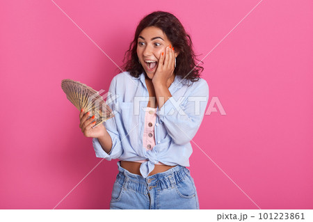 Portrait of shocked young brunette woman wearing casual clothes, female holding fan of cash money, has surprised facial expression, isolated over pink background in studio. People lifestyle concept. Portrait of shocked young brunette woman wearing casual clothes, female holding fan of cash money, has surprised facial expression, isolated over pink background in studio. People lifestyle concept. 101223861