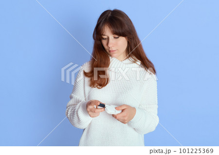 Woman holding electronic cigarette, looking down at device, female wearing white jumper, smoking e ciggy as alternative tobacco, young girl with bad habits choosing disjunctive. Woman holding electronic cigarette, looking down at device, female wearing white jumper, smoking e ciggy as alternative tobacco, young girl with bad habits choosing disjunctive. 101225369