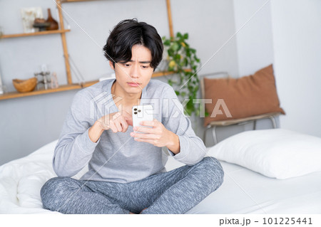 ベッドでスマホを見る若い男性 101225441