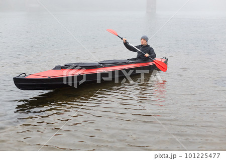 Concentrated man with oar in hands rowing boat in river in cold autumn day, water sport, guy wearing grey cap and and black jacket spending his spare time in active way. Concentrated man with oar in hands rowing boat in river in cold autumn day, water sport, guy wearing grey cap and and black jacket spending his spare time in active way. 101225477