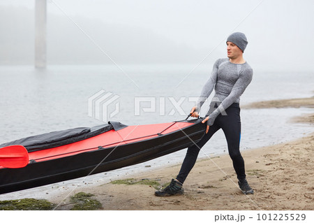 Handsome strong man pulling his boat from water, wearing sporty wear, pudding on lake, water sport in early foggy morning in autumn. 101225529