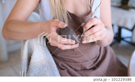 a woman processes a clay bowl with tools. 101229386