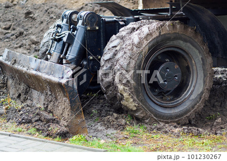 Wheeled tractor with shovel clears ground on cloudy rainy day. Dirty bulldozer shovel close-up.. Wheeled tractor with shovel clears ground on cloudy rainy day. Dirty bulldozer shovel close-up.. 101230267