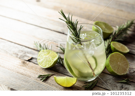 Gin tonic with ice, rosemary, and lime slices on an old wooden table. Gin tonic with ice, rosemary, and lime slices on an old wooden table. 101235312