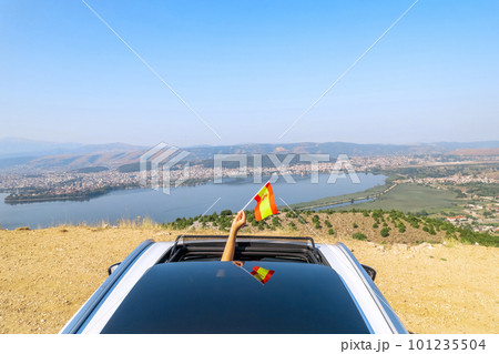 Woman holding Spain flag from the open car sunroof,  window driving along the serpentine road in the mountains. Top view.  Concept 101235504