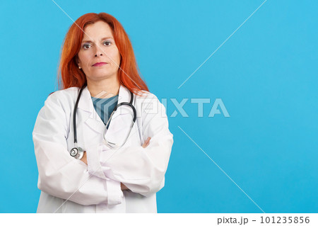 Serious mature redheaded female doctor standing with arms crossed Serious mature redheaded female doctor standing with arms crossed 101235856