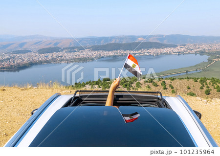 Woman holding Egypt flag from the open car sunroof, window driving along the serpentine road in the mountains. Top view. Concept Woman holding Egypt flag from the open car sunroof, window driving along the serpentine road in the mountains. Top view. Concept 101235964