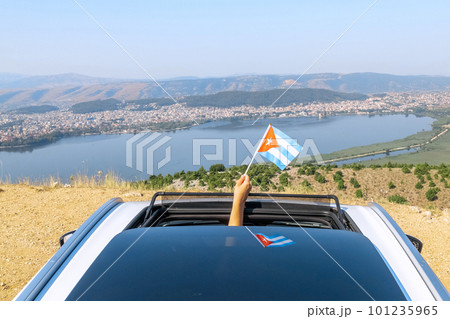 Woman holding Cuba flag from the open car sunroof,  window driving along the serpentine road in the mountains. Top view.  Concept 101235965