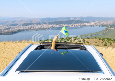 Woman holding Brazil flag from the open car sunroof,  window driving along the serpentine road in the mountains. Top view. Concept 101235982