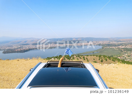 Woman holding Greece flag from the open car sunroof,  window driving along the serpentine road in the mountains. Top view. Concept 101236149