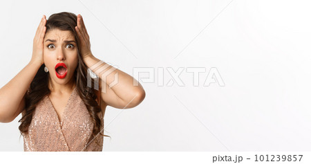 Concept of New Year celebration and winter holidays. Close-up of woman in luxury dress looking shocked and worried, standing over white background Concept of New Year celebration and winter holidays. Close-up of woman in luxury dress looking shocked and worried, standing over white background 101239857